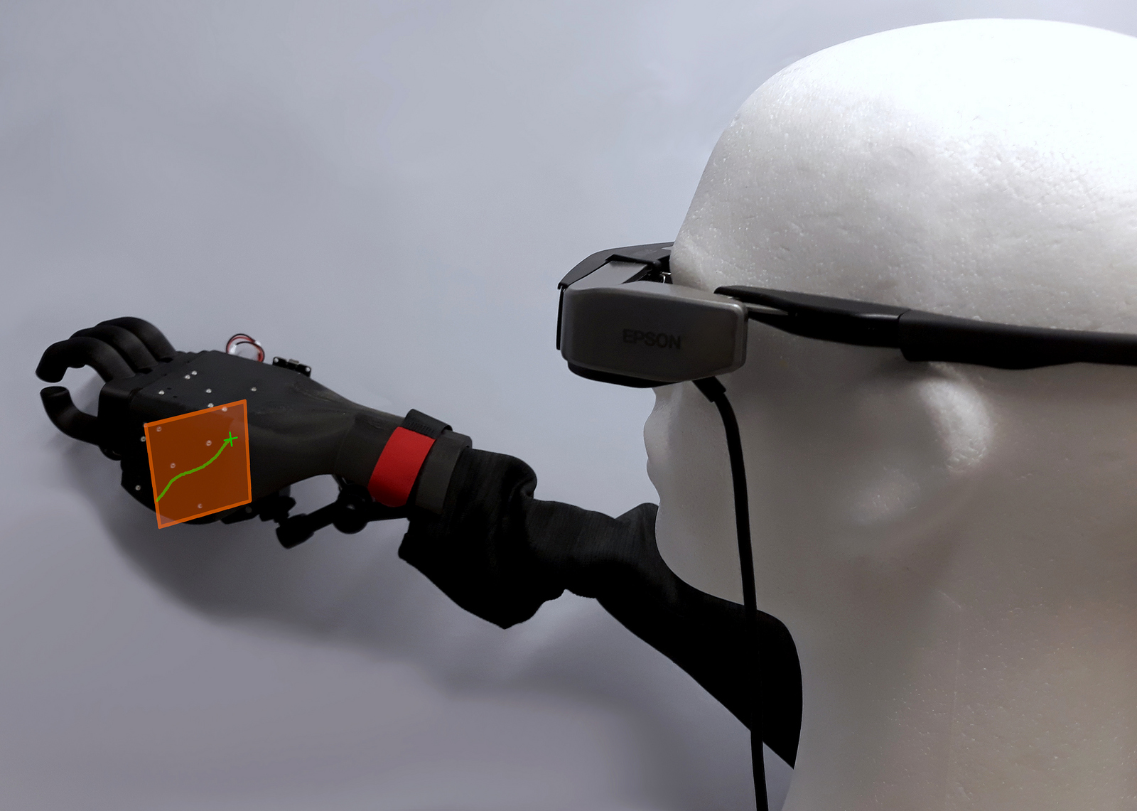 Ein Styroporkopf mit einer AR-Brille und eine Handprothese die an eine Wand greift 